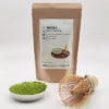 Premium grade Japanese Matcha powder displayed in a dish with a bamboo whisk, next to J-okini’s 100g Matcha package. Pesticide-free and perfect for traditional tea, Matcha lattes, and sweets. Available at j-okini.com in Malta