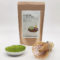 Premium grade Japanese Matcha powder displayed in a dish with a bamboo whisk, next to J-okini’s 100g Matcha package. Pesticide-free and perfect for traditional tea, Matcha lattes, and sweets. Available at j-okini.com in Malta