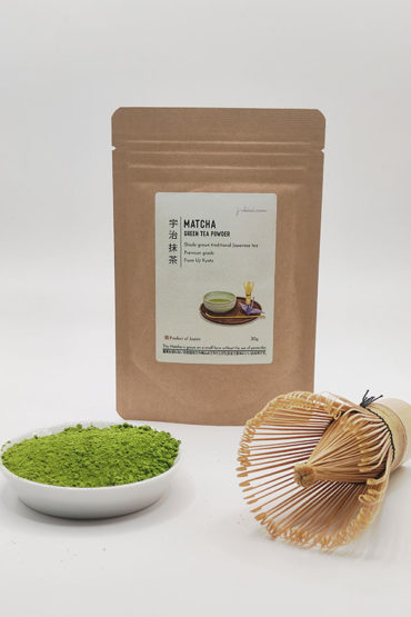 Premium grade Japanese Matcha powder displayed in a dish with a bamboo whisk, in front of J-okini’s 30g Matcha package. Pesticide-free and perfect for traditional tea, Matcha lattes, and sweets. Available at j-okini.com in Malta