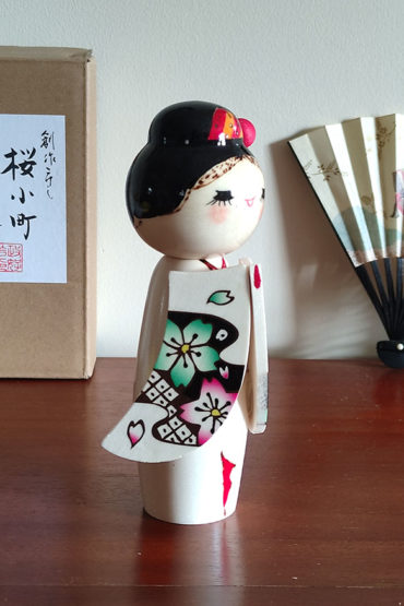 Handcrafted Japanese Kokeshi doll 'Sakura Komachi' by artist Yamagishi Masayoshi, featuring a kanzashi hair bun and a kimono with hand-painted pink and blue cherry blossoms. Available at j-okini.com in Malta
