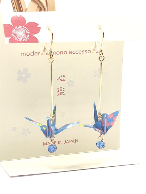 Crafted with meticulous attention to detail, these earrings feature a 3cm piece of Chiyogami, a traditional Japanese washi paper, known for its vibrant and intricate designs. Each pair is carefully sealed with three layers of protective coating to ensure durability and shine. At the heart of these earrings is the motif of the Tsuru, the Japanese word for crane. Revered in Japanese culture, the Tsuru is celebrated as a symbol of peace and longevity, embodying wishes for prosperity and health. These earrings are not only a testament to unique craftsmanship but also carry a deep cultural significance. The design is complemented by a delicate blue glass bead, harmonizing beautifully with the blue Chiyogami paper to create a piece that is both eye-catching and meaningful. Made in Japan. Available at j-okini.com