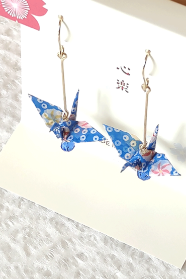 Crafted with meticulous attention to detail, these earrings feature a 3cm piece of Chiyogami, a traditional Japanese washi paper, known for its vibrant and intricate designs. Each pair is carefully sealed with three layers of protective coating to ensure durability and shine. At the heart of these earrings is the motif of the Tsuru, the Japanese word for crane. Revered in Japanese culture, the Tsuru is celebrated as a symbol of peace and longevity, embodying wishes for prosperity and health. These earrings are not only a testament to unique craftsmanship but also carry a deep cultural significance. The design is complemented by a delicate blue glass bead, harmonizing beautifully with the blue Chiyogami paper to create a piece that is both eye-catching and meaningful. Made in Japan. Available at j-okini.com