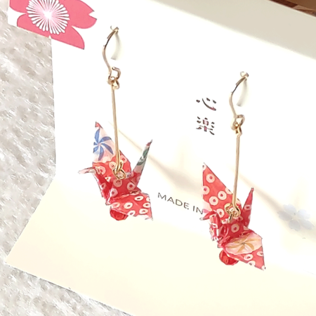 Crafted with meticulous attention to detail, these earrings feature a 3cm piece of Chiyogami, a traditional Japanese washi paper, known for its vibrant and intricate designs. Each pair is carefully sealed with three layers of protective coating to ensure durability and shine. At the heart of these earrings is the motif of the Tsuru, the Japanese word for crane. Revered in Japanese culture, the Tsuru is celebrated as a symbol of peace and longevity, embodying wishes for prosperity and health. These earrings are not only a testament to unique craftsmanship but also carry a deep cultural significance. The design is complemented by a delicate red glass bead, harmonizing beautifully with the pink Chiyogami paper to create a piece that is both eye-catching and meaningful.
