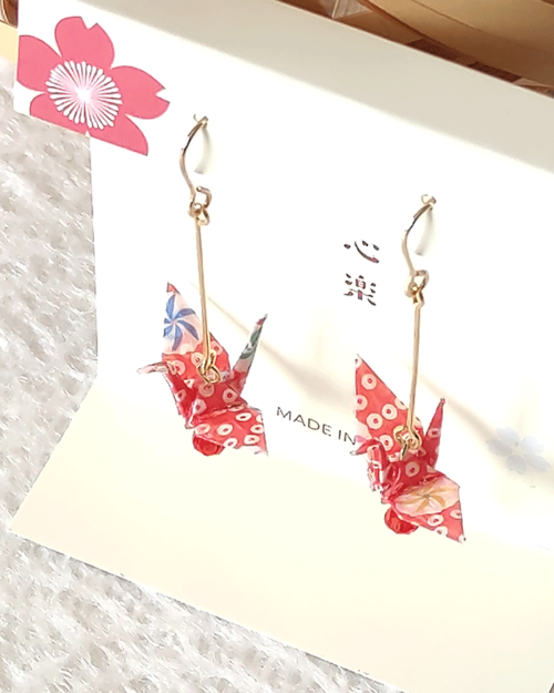 Crafted with meticulous attention to detail, these earrings feature a 3cm piece of Chiyogami, a traditional Japanese washi paper, known for its vibrant and intricate designs. Each pair is carefully sealed with three layers of protective coating to ensure durability and shine. At the heart of these earrings is the motif of the Tsuru, the Japanese word for crane. Revered in Japanese culture, the Tsuru is celebrated as a symbol of peace and longevity, embodying wishes for prosperity and health. These earrings are not only a testament to unique craftsmanship but also carry a deep cultural significance. The design is complemented by a delicate red glass bead, harmonizing beautifully with the pink Chiyogami paper to create a piece that is both eye-catching and meaningful.