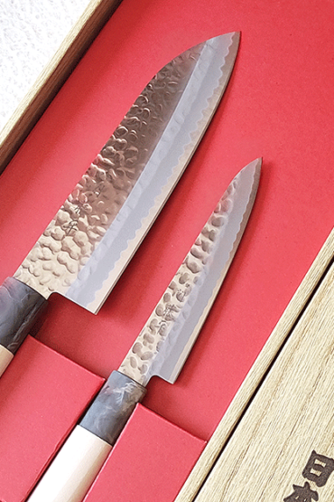 Yaxell, a revered name in the world of fine Japanese cutlery since 1932, presents a gift set that embodies the spirit of Gifu and Seki's legendary knife-making tradition. These regions are celebrated for producing some of the most sought-after kitchen knives, known for their auspicious qualities and unparalleled craftsmanship. The signature 関藤平 mark on every knife is a testament to its authenticity and heritage, ensuring you own a piece of Japanese history. Blade It features a beautiful hammered design and provides comfortable cutting. Handle Both knives feature handles made from magnolia wood, renowned for its beauty and durability. This gift set includes: 1. 三得包丁 Santoku Bocho Overall length 295mm Blade length 165mm Weight: 79g The Santoku Bocho is the epitome of versatility, designed to handle all types of food with ease. Its balanced weight and size make it the perfect tool for any culinary challenge, embodying the harmony of traditional Japanese craftsmanship and modern needs. 2.ペティ petty Overall length 235mm Blade length 120mm Weight: 44g The Petty knife, a compact counterpart of the ‘Gyutou’, offers exceptional maneuverability and precision. Ideal for intricate tasks, its small size and sharp edge allow for detailed work, making it an indispensable tool in any kitchen.. Available at j-okini.com in Malta