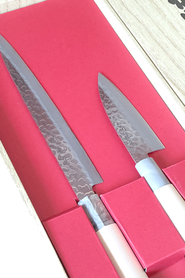 Gift masterpieces of Gifu and Seki of Japan. Yaxell is one of the major knife manufacturers in Japan since 1932, each Yaxell knife is a testament to the artistry and meticulous craftsmanship that has defined Japanese knife-making for generations, making them not just tools, but auspicious gifts that symbolize good fortune and prosperity. Made by Seki Tohei, and there are sign of 関藤平 on each knife. Blade It features a striking hammered design and provides comfortable cutting. Handle Sculpted from natural wood, designed to harmonize with your grip over time, becoming an extension of your culinary expression. This natural material not only adds to the knife's aesthetic but ensures durability and comfort with every use. This gift set includes: 1. 刺身包丁 Sashimi Bocho Overall length 330mm Blade length 205mm Weight: 79g Designed for precision, the Sashimi Bocho is the epitome of Japanese culinary artistry. Its long, slender blade is crafted to execute the most delicate and thin slices, perfect for sashimi, showcasing the knife's blend of functionality and elegance. 2.小出刃包丁 Small deba bocho Overall length 220mm Blade length 105mm Weight: 44g Specialized for handling smaller fish, this knife combines robustness and precision. Its compact design and sharp edge make it ideal for detailed work, from filleting to intricate cuts, embodying the spirit of traditional Japanese fish preparation.. Available at j-okini.com Malta