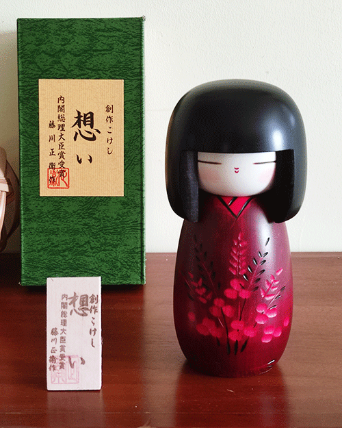 Crafted by the distinguished artist 藤川正衛 Fujikawa Shoei, the '想い Omoi' Kokeshi doll embodies the essence of heartfelt emotions, desires, and wishes. This award-winning piece captivates with its chic red kimono, intricately carved with delicate flowers and leaves, symbolizing the transmission of deep feelings. The doll's unique design features a slightly wider head, meticulously balanced with the dimensions of her eyes, hair length, and body, creating a harmonious and visually appealing figure. '想い Omoi' stands as a testament to traditional craftsmanship infused with the profound depth of human emotions. Available at j-okini.com in Malta