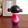 This 近代創作こけし modern creative Kokeshi doll is called 'うららか（おだんご）- Uraraka (Odango)' and it was created by an award-winning artist 'ちえ Chie'. The doll's feature would be the space buns.  Her Kimono has a design of Sakura (cherry blossoms) and the gradation of red to purple is beautiful. Find it at j-okini.com in Malta