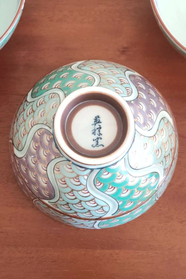 This exquisite Japanese rice bowl exemplifies the rich, over 400-year tradition of Arita ware, renowned for its timeless beauty and expert craftsmanship. Handcrafted in the famed pottery region of Arita, Japan, the bowl features a stunning 青海波 (Seigaiha) wave pattern in shades of green and purple, elegantly traced with gold accents.  The rim is adorned with intricate navy blue detailing, enhancing the bowl’s overall sophistication. Each bowl is meticulously hand-painted, showcasing the artistry and skill of the craftsmen who continue to honor Arita's proud ceramic heritage. Its versatile size makes it ideal for serving rice, soups, or even desserts, adding a refined touch to any meal. Made in Japan What is the Seigaiha Pattern? The 青海波 (Seigaiha), or "blue ocean wave" pattern, is a traditional Japanese motif symbolizing the calm and endless waves of the sea. This auspicious design is believed to represent a wish for a peaceful and prosperous life. Available at j-okini in Malta