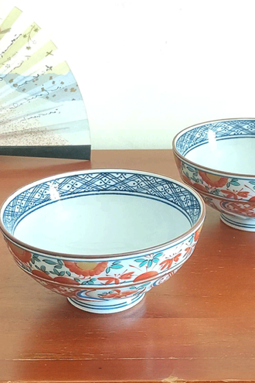 This exquisite Japanese rice bowl embodies the rich, 400-year legacy of Arita ware, celebrated for its timeless elegance and masterful craftsmanship. Handcrafted in the renowned pottery region of Arita, Japan, this bowl showcases the traditional Aka-e technique, a style known for its vibrant use of red, green, and blue hues.  The intricate design combines delicate floral motifs with geometric patterns, while the rim is beautifully accented with navy blue detailing, adding a layer of sophistication to the piece. Each bowl is meticulously hand-painted, reflecting the artistry and dedication of Arita’s skilled craftsmen, who continue to uphold this centuries-old ceramic tradition. Its versatile size makes it perfect for serving rice, soups, or desserts, bringing a refined touch of Japanese artistry to any meal.
