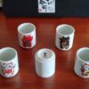 A 5-piece Mino ware sake cup set featuring colorful Maneki-Neko designs, each representing luck, protection, or prosperity. Available at j-okini.com in Malta