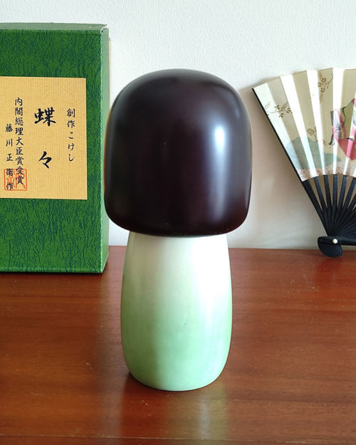 Handcrafted Japanese Kokeshi doll 'Chouchou' by artist Fujikawa Shoei, featuring a light green Michiyuki kimono jacket with a butterfly and pink floral design. Available at j-okini.com in Malta