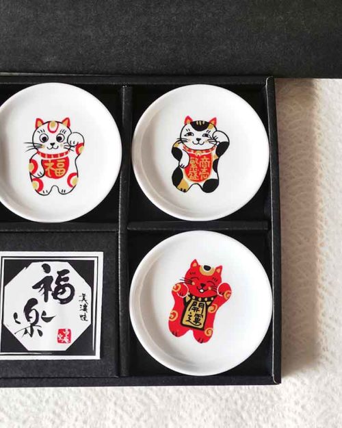 A set of five Japanese Maneki-Neko small dishes, each featuring a unique beckoning cat design symbolizing luck, protection, happiness, prosperity, and wealth. Perfect for serving soy sauce or condiments. Made in Japan. Available at j-okini.com in Malta
