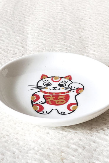 A charming Maneki-Neko small dish made from white porcelain, featuring a lucky cat with red and gold patches and the 福 (Fuku) character symbolizing happiness. Perfect for serving soy sauce or small appetizers, or as a decorative accent. Made in Japan, handcrafted Mino ware. Available at j-okini.com in Malta