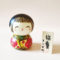 Ume Warabe Kokeshi doll by Toshio – green kimono with red plum blossoms. Buy it online at j-okini.com in Malta