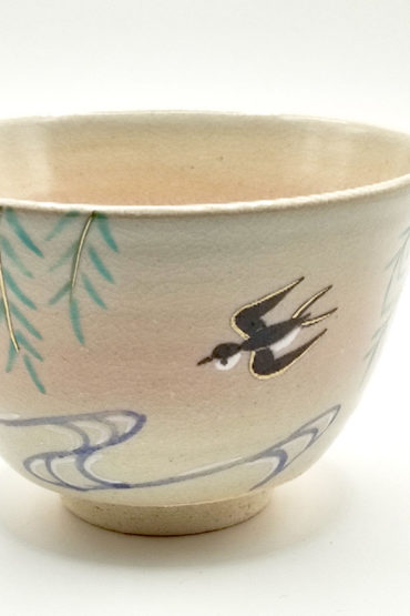 close up to Kiyomizu-ware matcha bowl “Yanagi to Tsubame” by Kahou Nakamura, featuring willow tree, sparrow in flight, flowing waves, gold details, and natural Gohonte patterns.