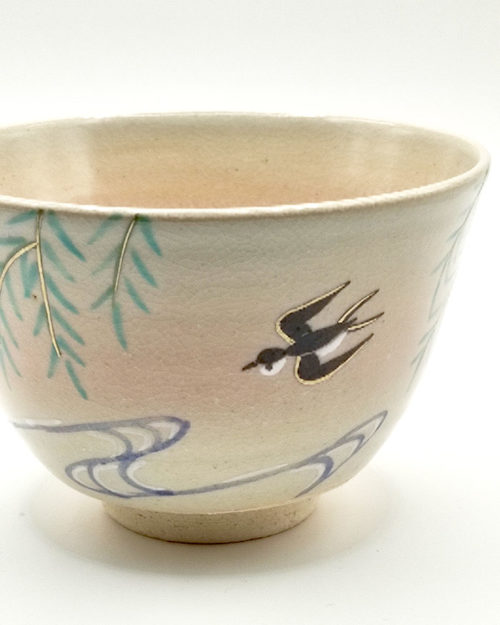 close up to Kiyomizu-ware matcha bowl “Yanagi to Tsubame” by Kahou Nakamura, featuring willow tree, sparrow in flight, flowing waves, gold details, and natural Gohonte patterns.