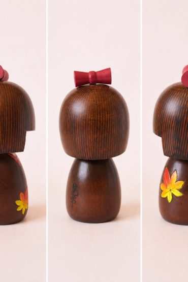 Kaede-chan Japanese wooden kokeshi doll by Kojo wearing a brown kimono decorated with yellow, orange and red maple leaves.