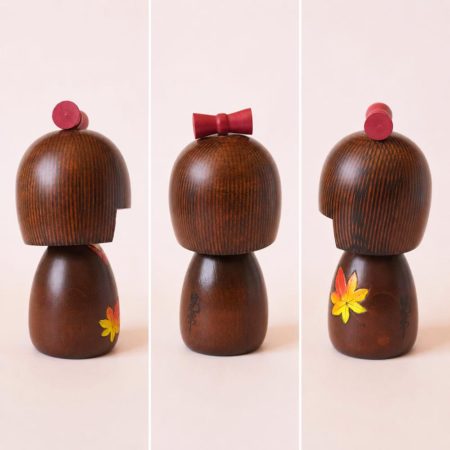 Kaede-chan Japanese wooden kokeshi doll by Kojo wearing a brown kimono decorated with yellow, orange and red maple leaves.