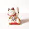 Small Japanese ceramic Maneki Neko lucky cat with raised paw, bell, colourful decorations and red cushion. Buy it on j-okini.com in Malta (Europe)