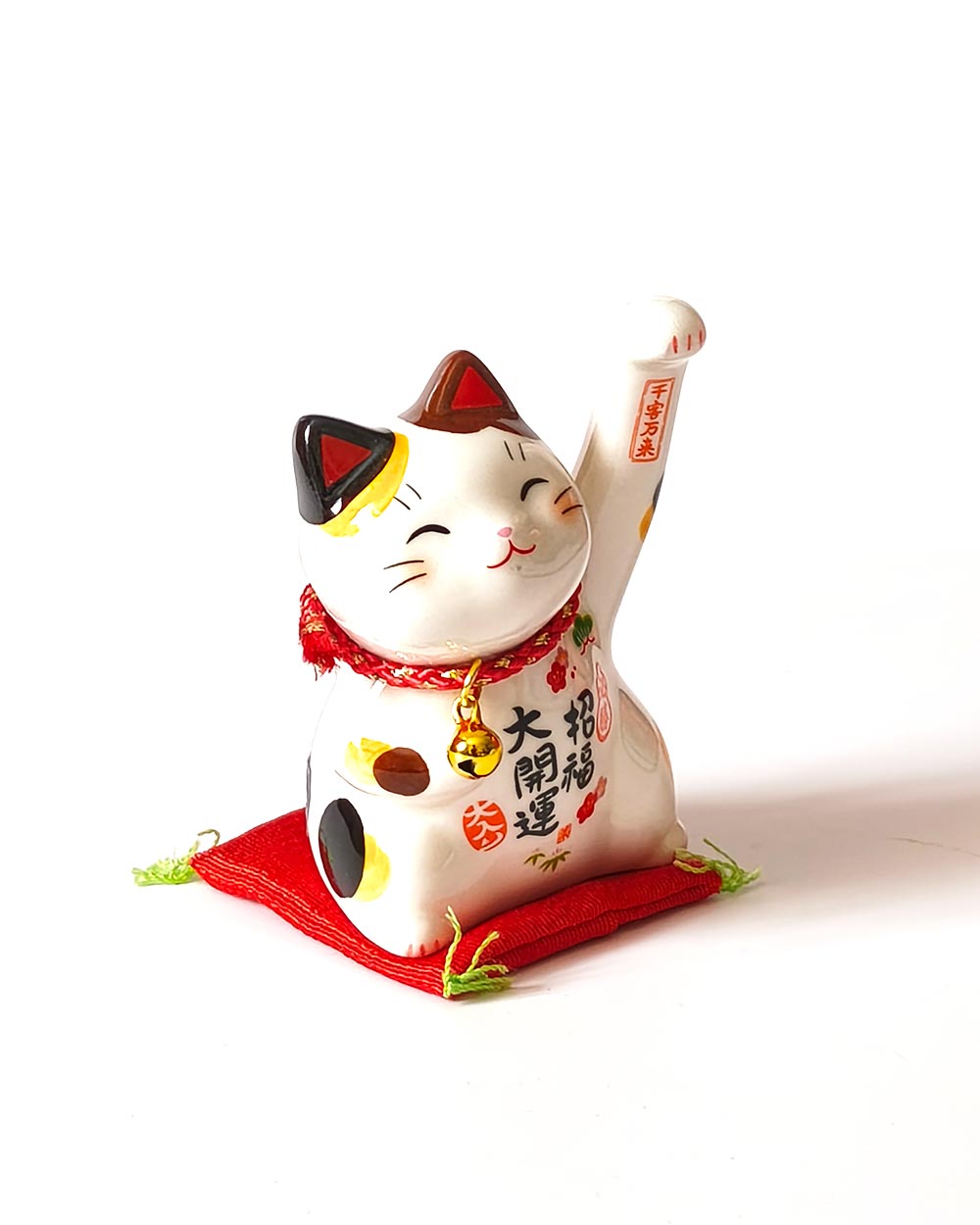 Japanese Lucky Maneki Neko Cat – Victory & Good Fortune (Small) Small Japanese ceramic Maneki Neko lucky cat with raised paw, bell, colourful decorations and red cushion. Buy it on j-okini.com in Malta (Europe)