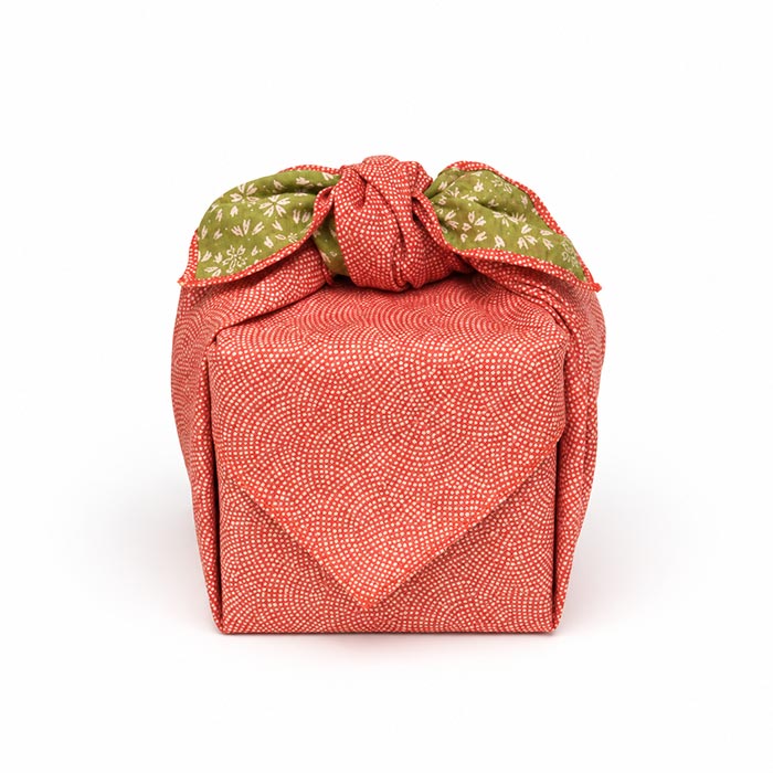 Japanese reversible cotton furoshiki tied around a gift, with a white dotted wave pattern on vermilion red and a green cherry blossom reverse visible at the knot.