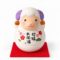 Round white Japanese zodiac sheep figurine with purple horns, floral decoration and Japanese good luck lettering, displayed on a red mat.